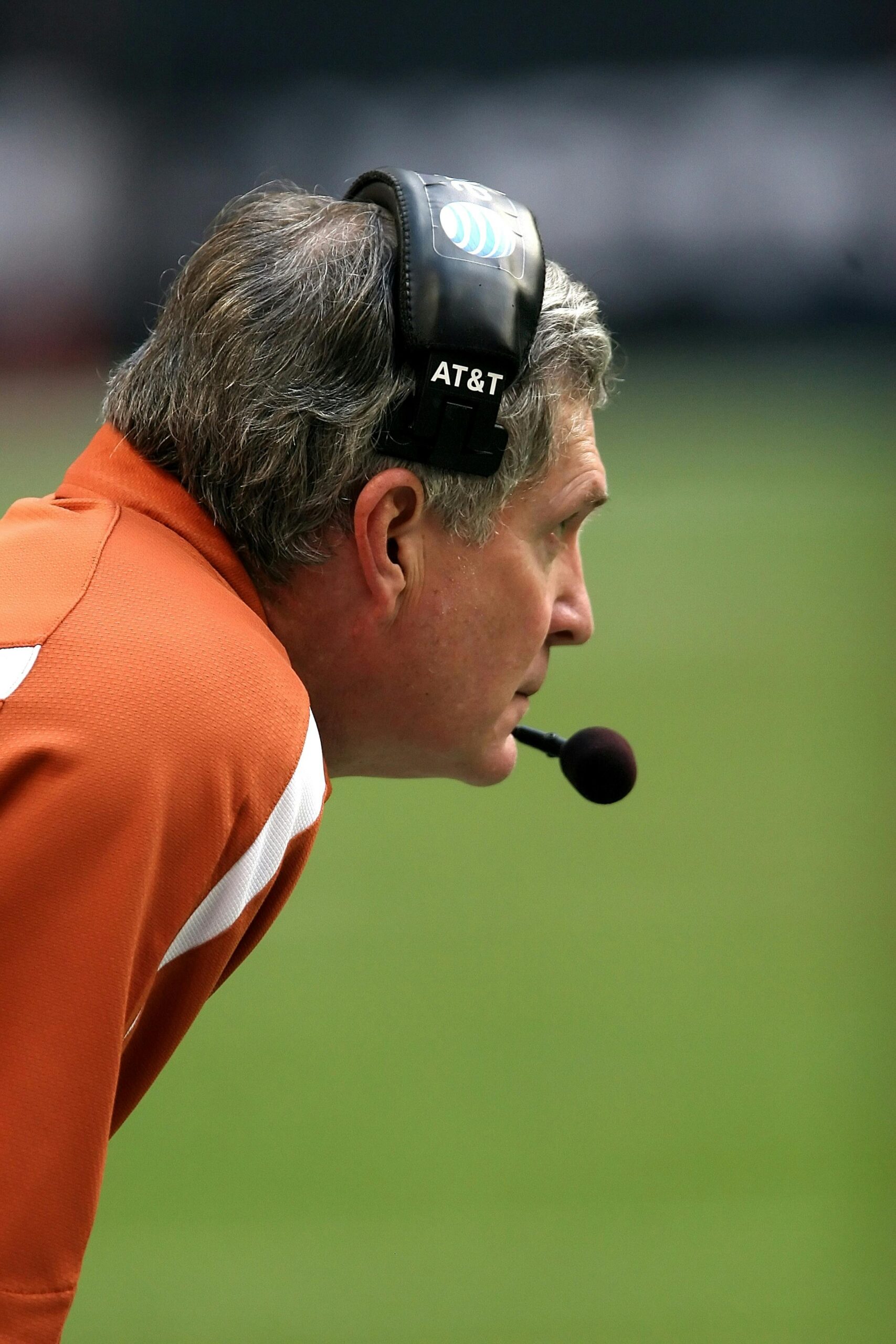 Side profile of a focused male football coach wearing a headset during a game.